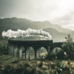 black train on railway bridge under heavy clouds