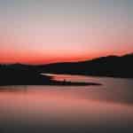 silhouette of mountain near body of water during sunset
